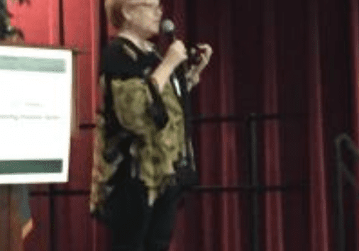 Person speaking on stage holding a microphone.