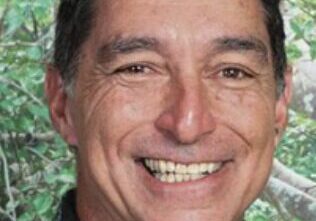 Smiling man in front of leafy background.