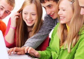Three teenagers happily looking at a laptop screen together.